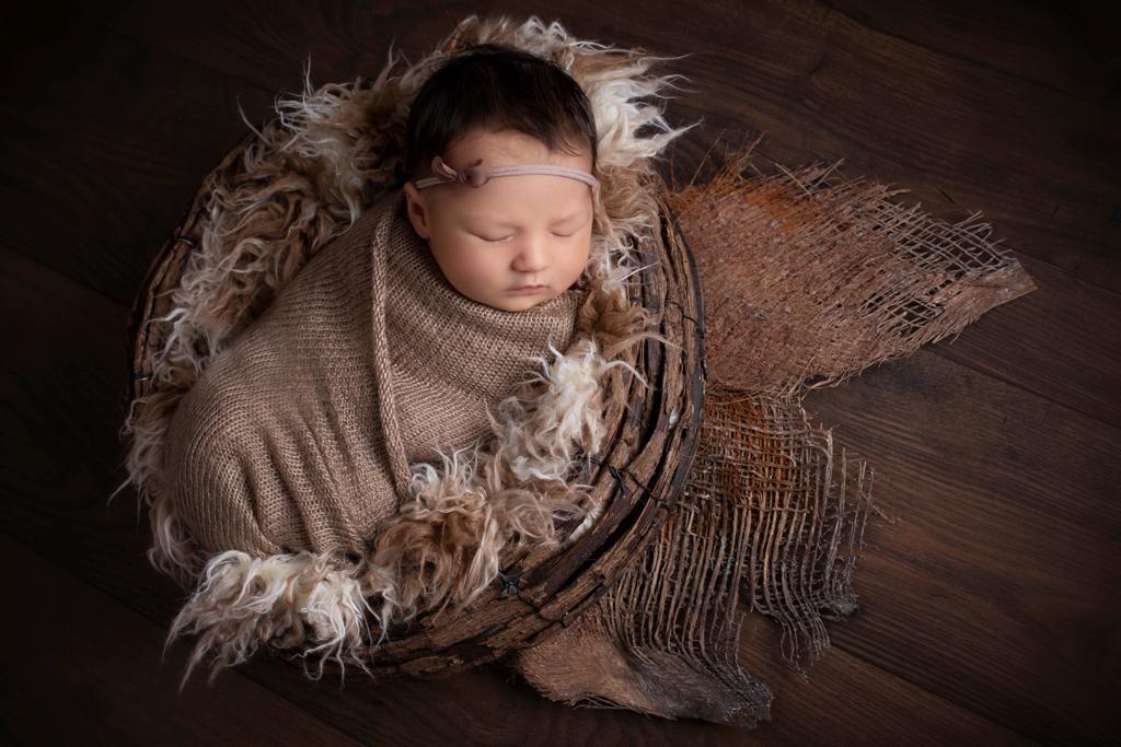 Babyfoto Düsseldorf: Baby liegt kuschelig gewickelt in einem Fell in einer Weidenschale. Herbststimmung.